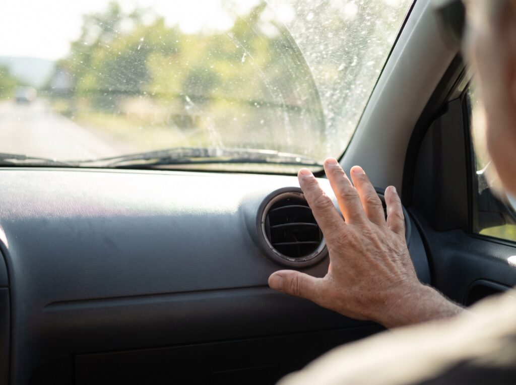Hand checking airflow from a car's dashboard vents on a hot Calgary summer day